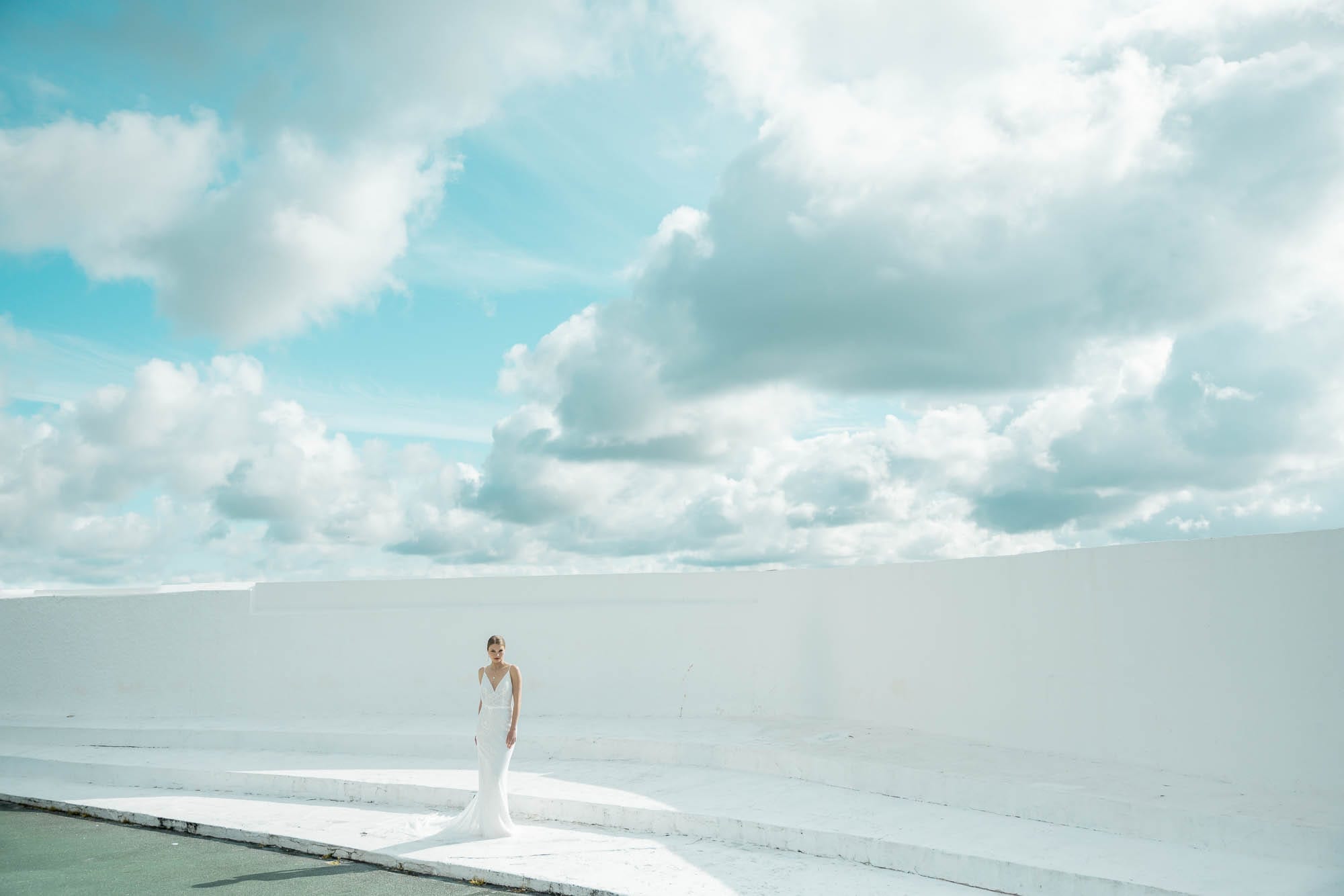 A bride stands alone in a vast white amphitheatre beneath a huge Cornish sky