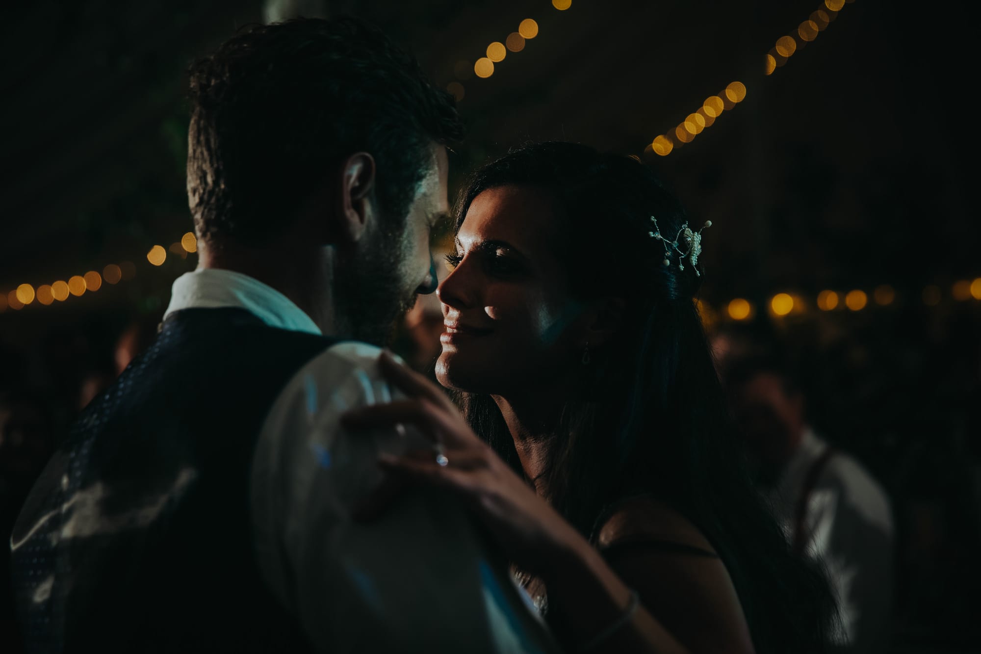 A bride watches her husband during the first dance under festoon lights in a Cornwall marquee